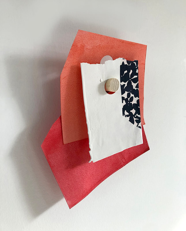 A three part peg drawing with a found floral dark blue and white dipped piece in front, and two shades of red hanging behind. 